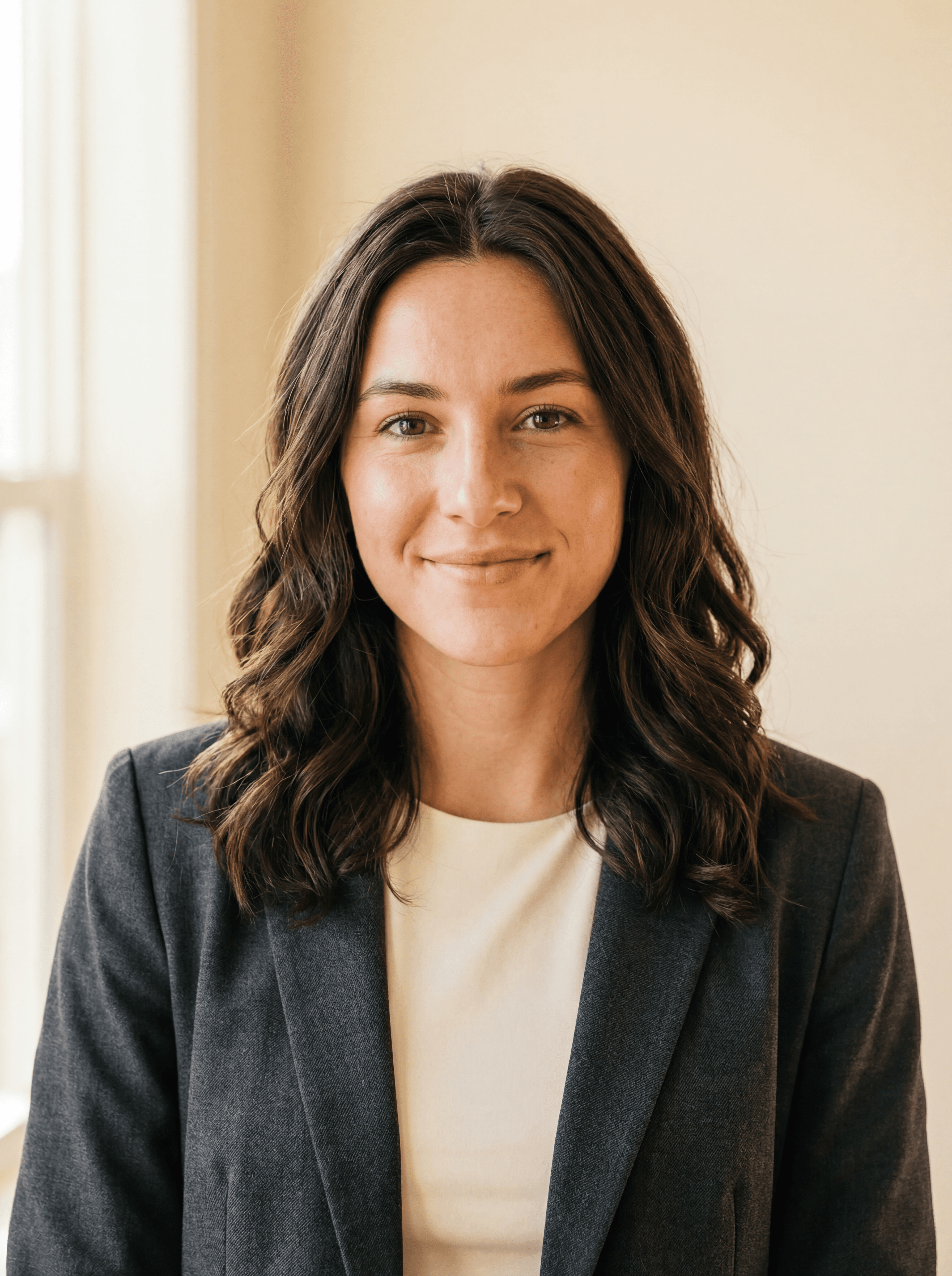 Same woman in a professional headshot wearing a dark blazer with soft studio lighting and a neutral beige background